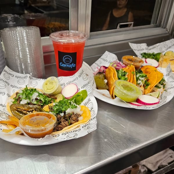 Two plates of Garrafa tacos with various toppings, sauces, and a red drink on a metal counter.