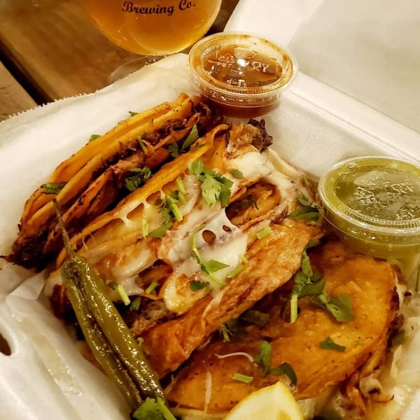 Garrafa's cheesy birria tacos with cilantro, lime, grilled peppers, and two sauces in a to-go container.