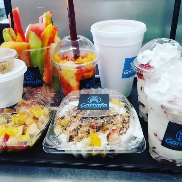 A variety of Garrafa Mexican fruit cups, yogurt parfaits, and drinks on a black tray.