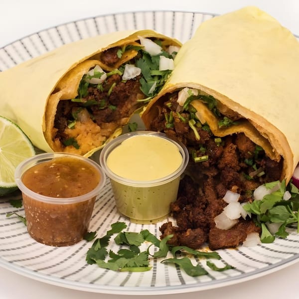 Two Garrafa burritos, one cut open, with lime, salsa, and guacamole on a striped plate.