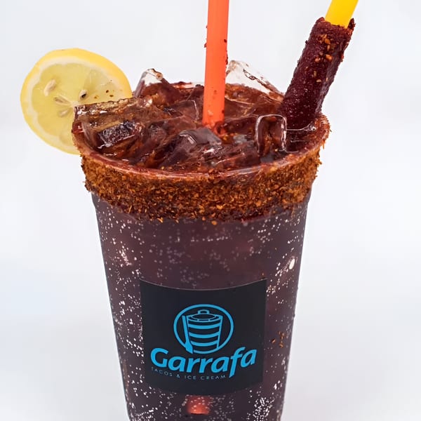 A Garrafa Mexican drink with a chili-lime rim, lemon slice, orange straw, and tamarind candy.